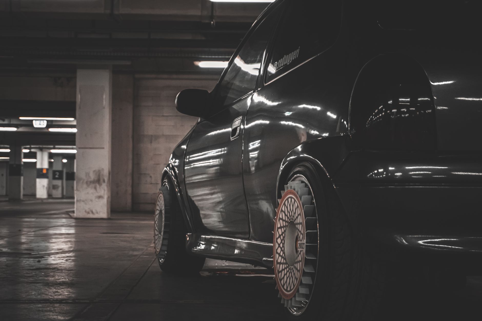 A dark saloon parked in the concrete studio, lit from one side