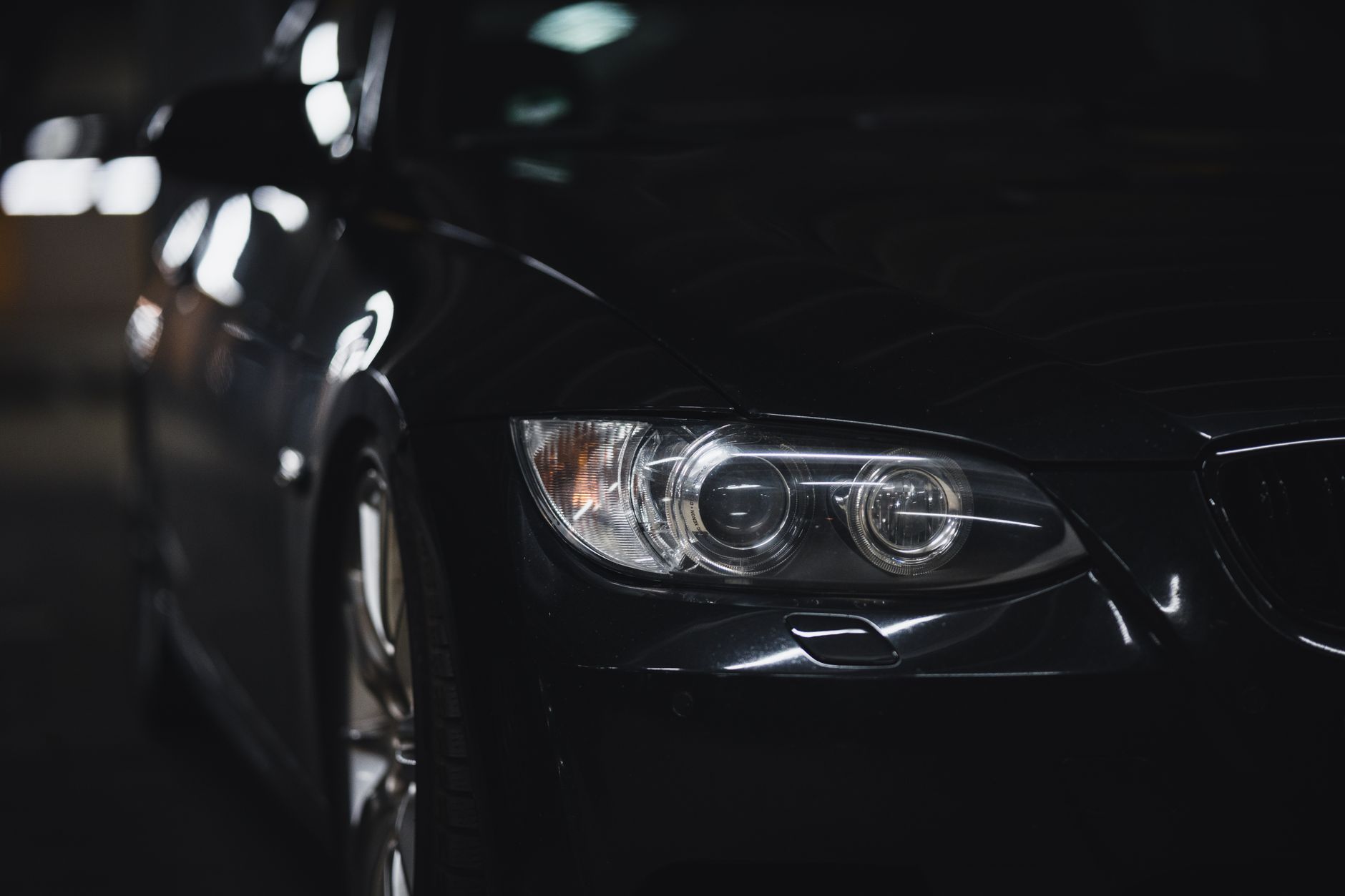 A black sedan headlight emerging from darkness in a dim studio